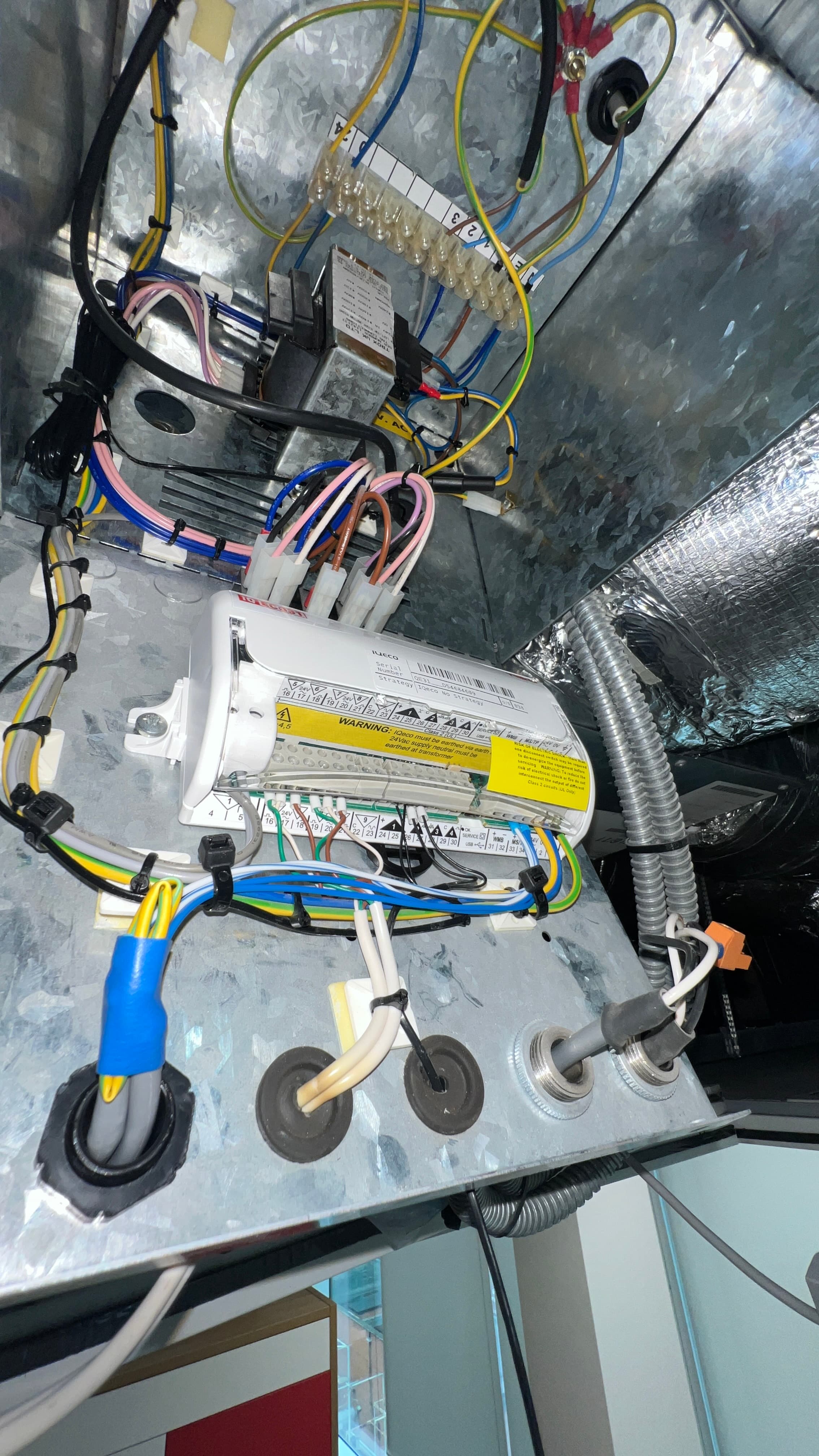 Trend IQeco controller with ferruled control wiring terminated at its terminal strip, mounted on galvanised sheet metal beside foil-faced insulation and flexible conduit