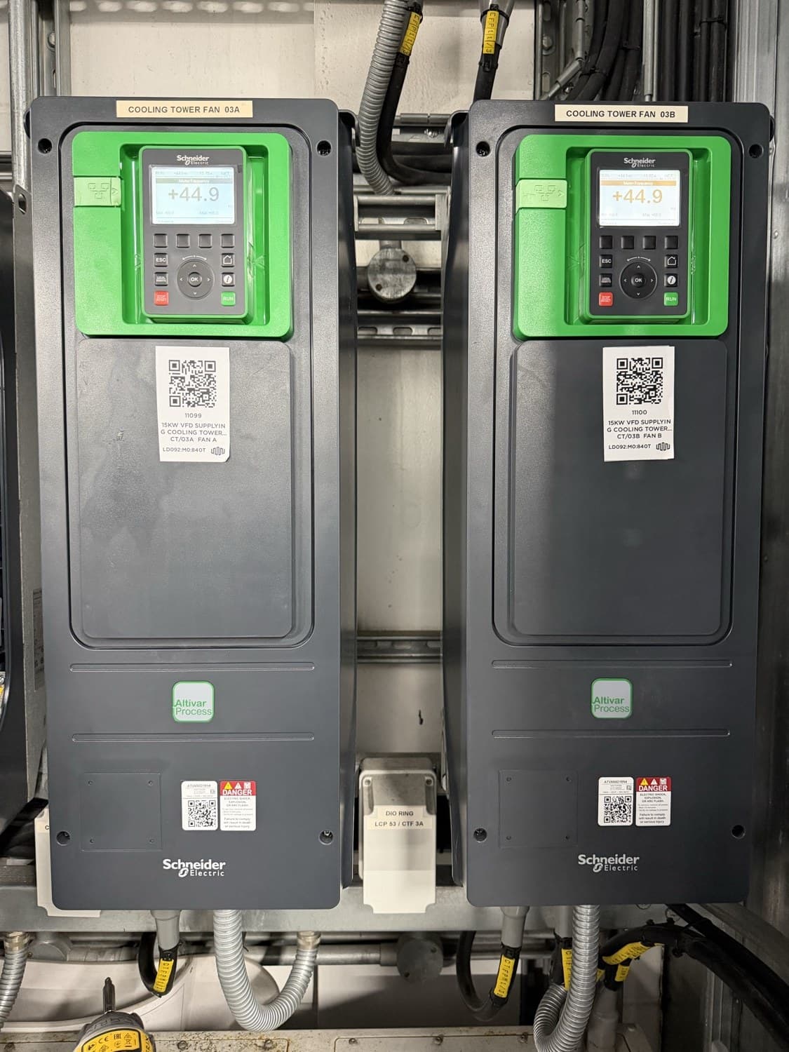 Two Schneider Altivar Process variable speed drives labelled Cooling Tower Fan 03A and 03B, displays lit and showing motor frequency, with flexible conduit entering below
