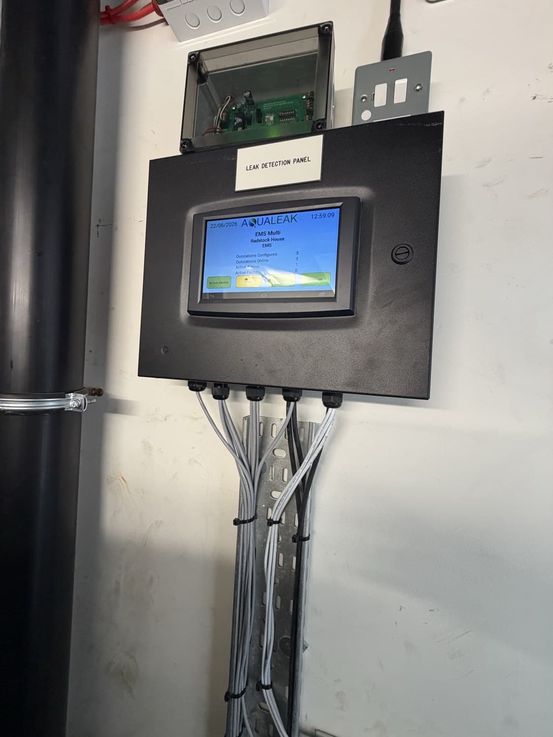 Wall-mounted Aqualeak leak detection panel with touchscreen display, cabled into containment below